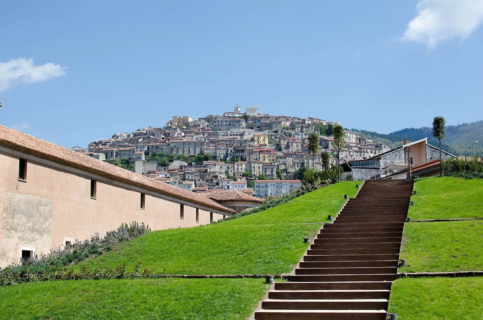 Il centro storico di Padula arroccato sulla collina, con prati verdi e una scalinata in primo piano